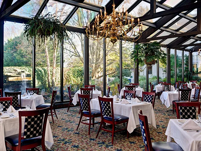 Glass-walled garden dining room with a brass chandelier and hanging ferns